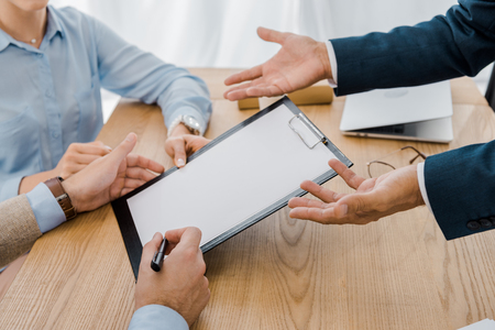 couple signing contract on clipboard with insurance agent at wooden tableの写真素材