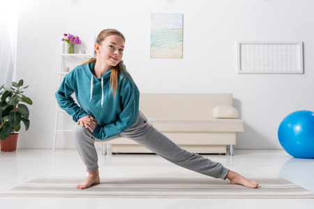 girl stretching legs on yoga mat and looking at camera at homeの写真素材