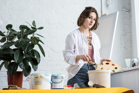 Young inspired girl holding palette and looking at camera in light studioの写真素材