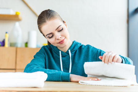 smiling young woman looking at white towels on tableの写真素材