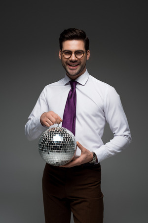 Smiling businessman holding glass disco ball isolated on greyの写真素材