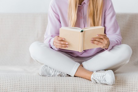 woman reading book and sitting on sofa with crossed legs