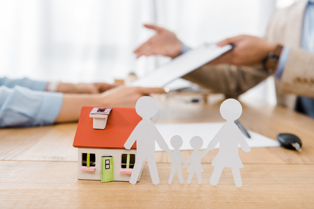 White paper cut family and house model on wooden table with blurred people at background, life and house insuranceの写真素材