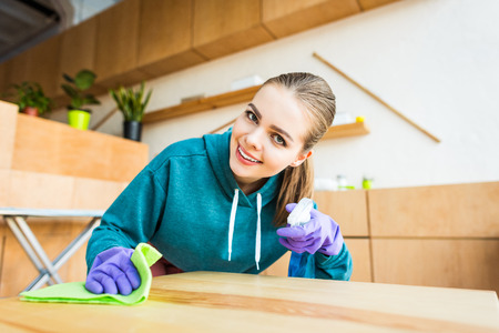 beautiful young woman smiling at camera while cleaning home with ragの写真素材