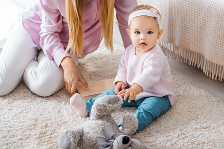 mother sitting on carpet with little daughter and playing with toyの写真素材