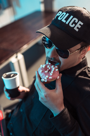 High angle view of prison guard eating doughnut and holding cup of coffeeの写真素材