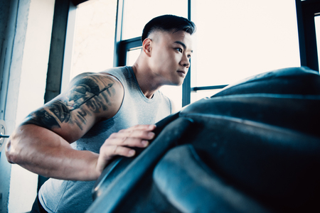 Handsome young sportsman flipping heavy tire at gymの写真素材