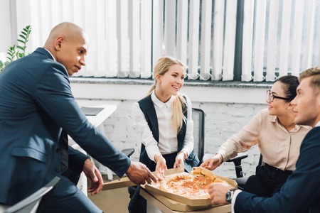 Happy young business people eating pizza together in officeの写真素材