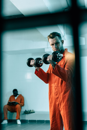 Prisoner training with dumbbells in prison room behind prison barsの写真素材