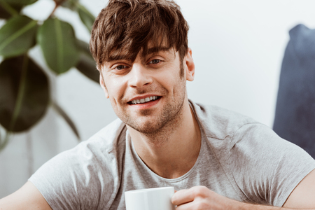 Portrait of smiling man looking at camera and drinking coffee at homeの写真素材