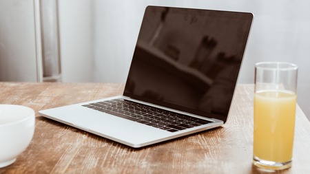 close up view of laptop with blank screen and orange juice at tableの写真素材