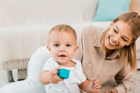 Adorable toddler looking at camera and playing with colorful cube and motherの写真素材