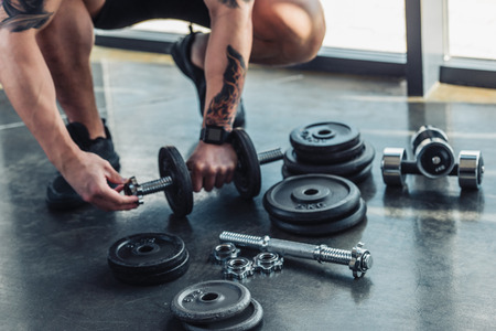 Partial view of tattooed sportsman assembling dumbbellsの写真素材