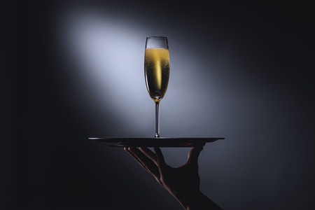 partial view of waitress holding serving tray with glass of champagne on dark backgroundの写真素材