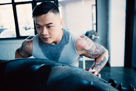 Close up of young Asian sportsman flipping heavy tire at gymの写真素材