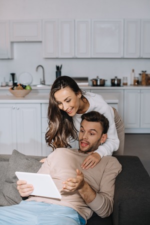 Happy young couple using tablet together on couch at homeの写真素材