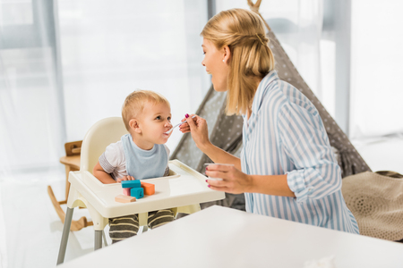 Mom feeding son in highchair with baby foodの写真素材