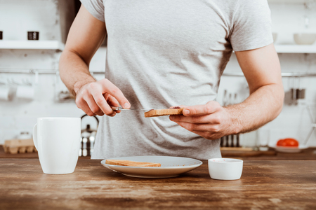 Cropped image of man spreading toast by jam in kitchen at homeの写真素材