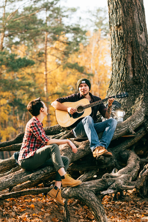 Happy woman and man having fun with guitar on autumal backgroundの写真素材