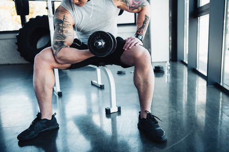 Partial view of young sportsman exercising with dumbbell in gym
