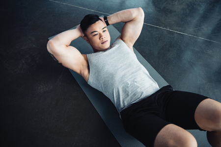 Young Asian sportsman doing abs exercise on fitness mat at gymの写真素材