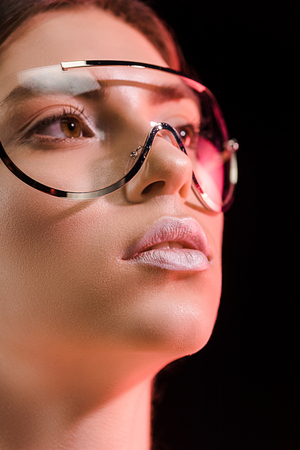 Portrait of beautiful woman in fashionable eyeglasses looking away isolated on blackの写真素材