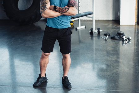 Cropped view of young sportsman with crossed arms at gymの写真素材