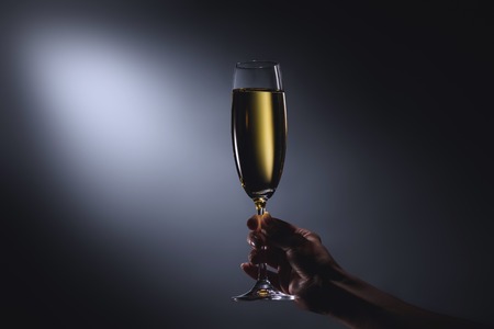 Partial view of woman holding glass of champagne in hand on dark backdropの写真素材