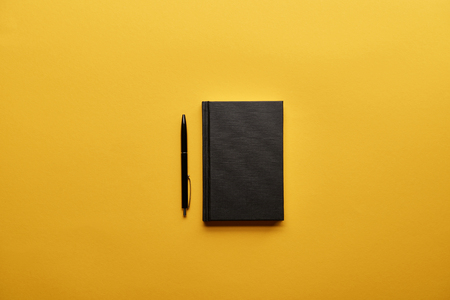 Top view of closed notebook and pen on yellow surfaceの写真素材