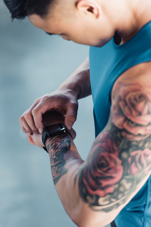 cropped view of young sportsman after long workout looking at watchの写真素材