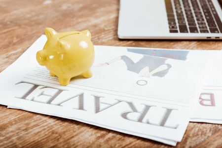 close up view of piggy bank on travel newspaper at table with laptop