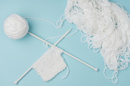 Top view of white yarn and knitting needles on pink backdrop