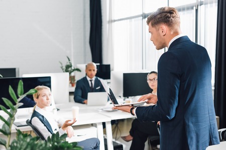 Serious young businessman using laptop and looking at colleagues in officeの写真素材