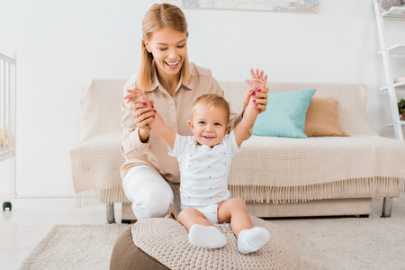Adorable toddler raising hands up with mother in nursery roomの写真素材