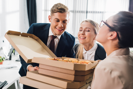 Happy young business colleagues smelling tasty pizza in office