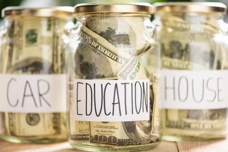 Close-up view of glass jars with dollar banknotes and inscriptions car, education, houseの写真素材