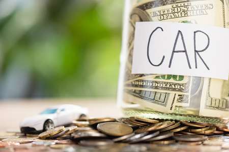 close-up view of glass jar with dollar banknotes and inscription car, coins and small car model on tableの写真素材