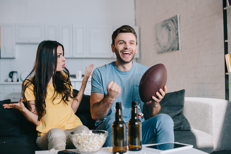 Angry young woman yelling at husband while he watching american football on tv at homeの写真素材