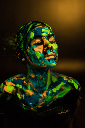 Portrait of woman painted with bright neon paints on dark backdropの写真素材