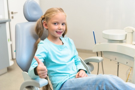 Beautiful little child sitting in dental chair at dentist office and showing thumb upの写真素材