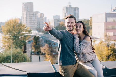 Beautiful young couple sitting on rooftop and looking somewhereの写真素材