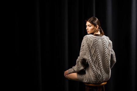 attractive pensive woman in woolen grey sweater on black backgroundの写真素材