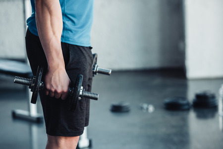 partial view of young sportsman exercising with dumbbells in gym