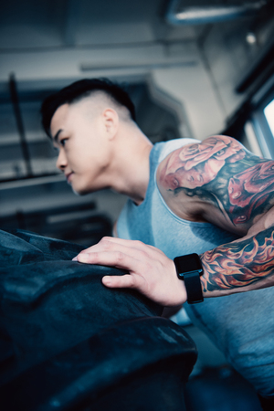 side view of young sportsman flipping heavy tire at gymの写真素材