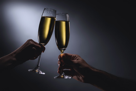 cropped shot of couple clinking glasses of champagne on dark background