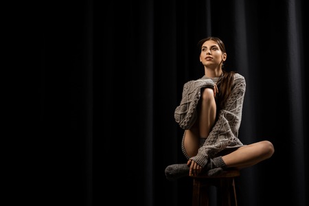 Beautiful pensive woman in woolen grey sweater and socks on black backgroundの写真素材