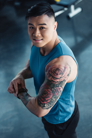 young tattooed asian sportsman at gym looking at cameraの写真素材
