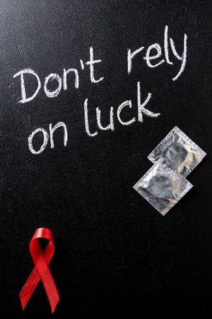 top view of aids awareness red ribbon and silver condoms on black backgroundの写真素材