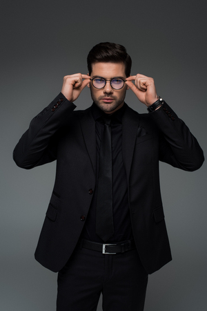 Man in stylish black suit taking off glasses isolated on greyの写真素材