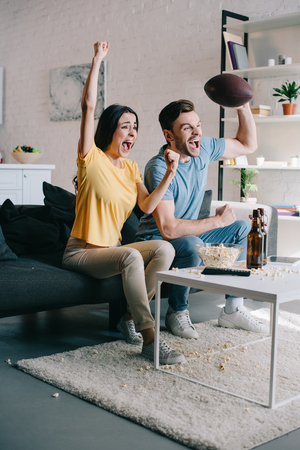 emotional young couple cheering for american football game at homeの写真素材